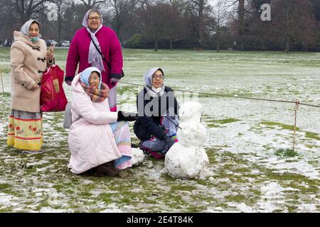 four ladies in head scarf having fun time with snowman in London greenwich park Stock Photo