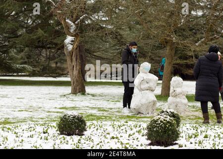 man in face mask building snowman in London Greenwich park Stock Photo