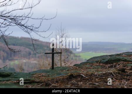 small iron cross on rock formation with blurry landscape in background Stock Photo