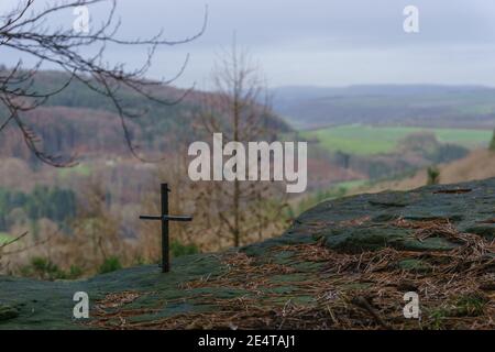 small iron cross on rock formation with blurry landscape in background Stock Photo