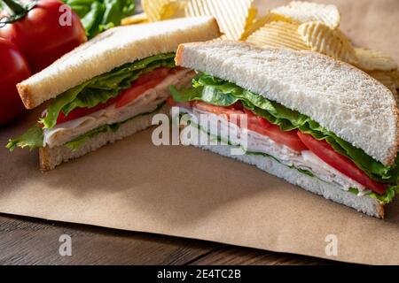 Fresh turkey, lettuce and tomato sandwich cut in half on brown paper Stock Photo