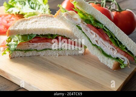 Fresh turkey, lettuce and tomato sandwich cut in half on cutting board Stock Photo