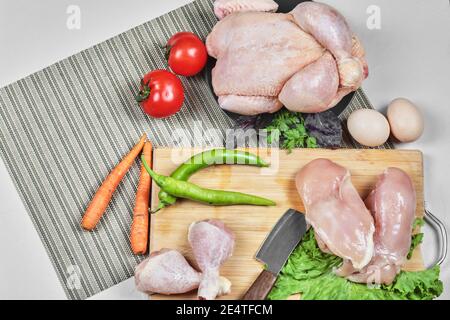 Raw chicken legs and fillet on wooden board with knife, eggs and fresh vegetables Stock Photo