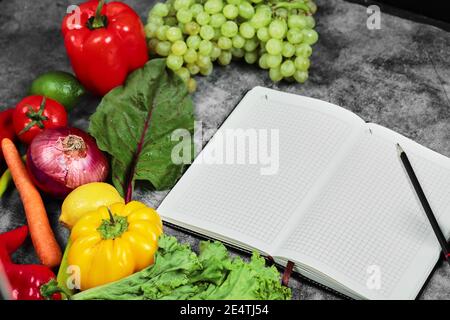 Grapes, peppers, greens, lemon, tomato and empty notebook on marble background Stock Photo