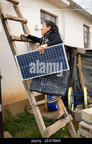 A technician from local non-profit power company installs a new solar powered lighting system on a home in Cantel, Guatemala. Stock Photo