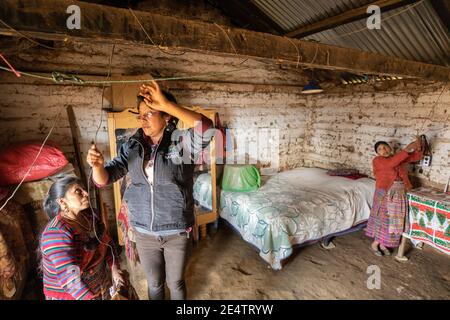 A technician from local non-profit power company installs a new solar powered lighting system in a home in Cantel, Guatemala. Stock Photo