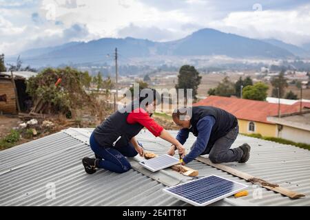 Technicians from local non-profit power company install a new solar powered lighting system on a home in Cantel, Guatemala, Cen Stock Photo