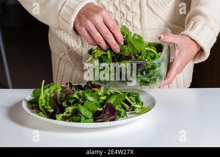 middle aged blonde woman preparing green salad in the kitchen, healthy eating and diet concept, close-up Stock Photo