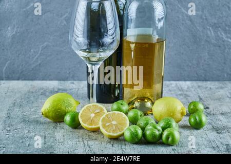 Two bottles and glass of wine on marble table with lemons and cherry plums Stock Photo