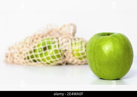 Green apples in eco mesh bag on white kitchen table. Market shopping. Food and Environment concept. Zero waste. Close up. Banner. Stock Photo
