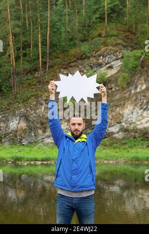 Young man standing on bank of river keeping blank white board in hands above his head. Your text here Stock Photo