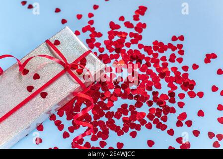 Valentine day silver gift box with red heart shaped glitter on blue background Stock Photo