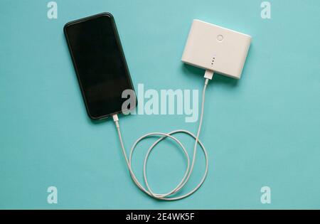 Cellphone getting charged from power bank. Isolated. On blue background. Stock Photo