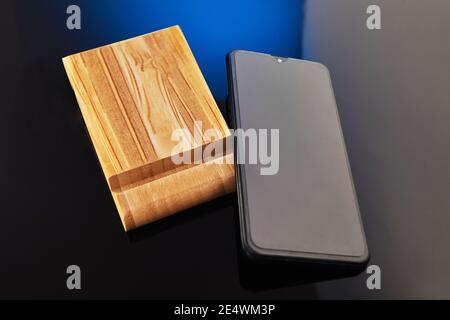 Wooden desktop mobile phone holder with hand-held phone isolated on blue black background. Creativity and technology concept Stock Photo