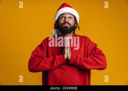Worried young african american man in santa claus hat asking for presents isolated on yellow background Stock Photo