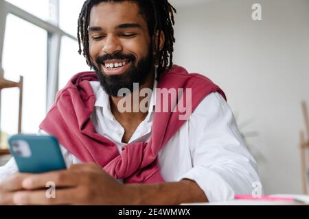Happy african american guy smiling and using cellphone while working in office Stock Photo