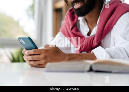 Happy african american guy smiling and using cellphone while working in office Stock Photo