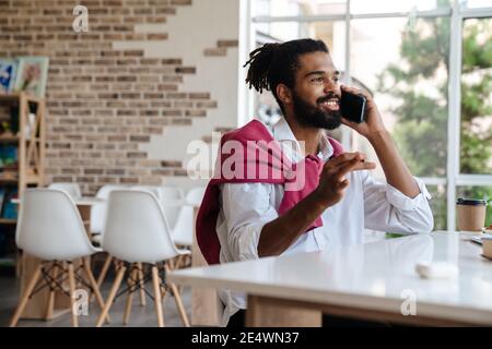 Smiling african american guy talking on cellphone and working in office Stock Photo