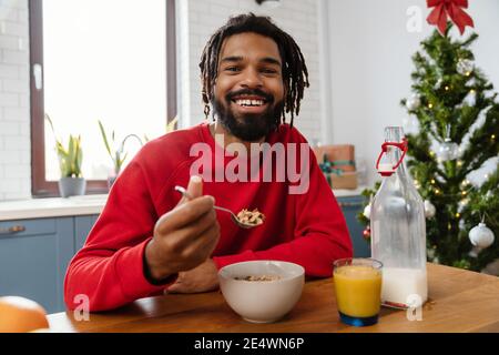Joyful african american man eating cereal while having breakfast in cozy kitchen Stock Photo