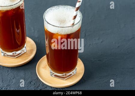 Ice coffee in tall glasses with ice on a black concrete background. Cold summer drink with paper straw. Stock Photo