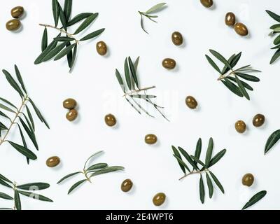 Beautiful pattern with green olives and olives tree leaves and branches on white background. Olive tree fruits and branches as pattern, top view or flat lay. Stock Photo