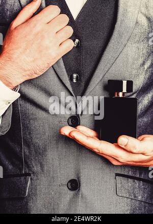 Fragrance smell. Men perfumes. Fashion cologne bottle. Man holding up bottle of perfume. Men perfume in the hand on suit background Stock Photo