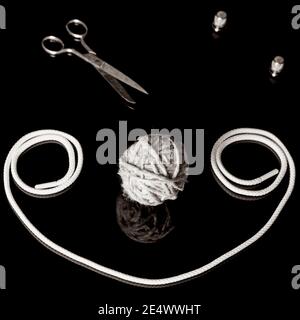 Black and white composition of a ball of twine, rope, scissors and steel sewing thimbles on a shiny reflective black background Stock Photo