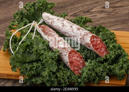 Spanish Fuet sausage with salad leaves over wooden background Stock Photo