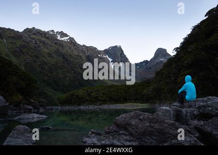 A tramper sitting on the rocks by the Lake Mackenzie at dawn, Routeburn Track, South Island Stock Photo