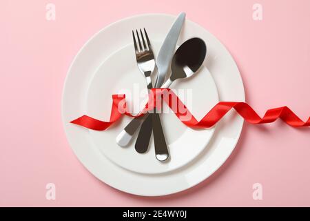 Plates with cutlery and red bow on pink background Stock Photo