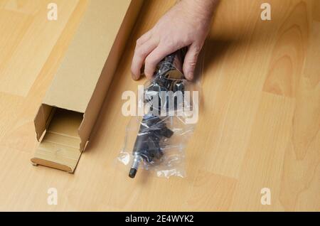 Continuous light photographic equipment, softbox. Hand places a new black softbox tripod in clear packaging next to the cardboard box. Stock Photo