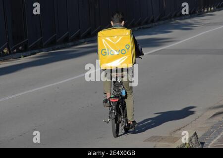 Rear view of a worker of Glovo food delivery courier. He is going down by bike along the street alone. Stock Photo