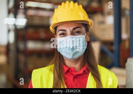 Happy Latin woman working in warehouse while wearing face mask during corona virus pandemic - Logistic and industry concept Stock Photo