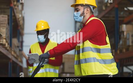 Team working in warehouse doing inventory using digital tablet loading delivery boxes while wearing face mask during corona virus pandemic Stock Photo