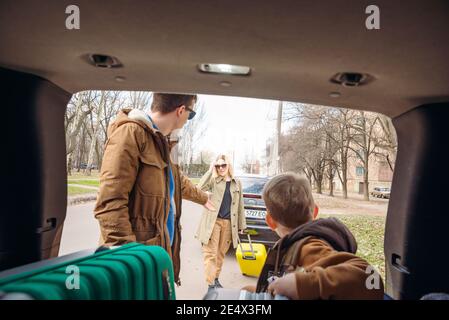 family with kid putting bag in car trunk. road trip gathering Stock Photo