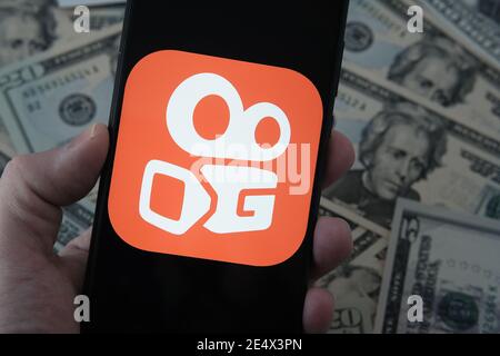 Stafford, United Kingdom - January 25 2021: Kuaishou app logo seen on the smartphone screen and blurred dollar banknotes on the background. Concept fo Stock Photo