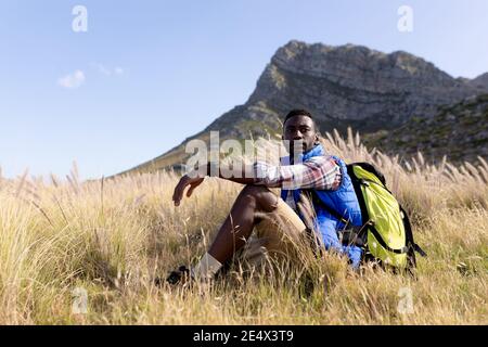Fit afrcan american man wearing backpack sitting in mountain countryside Stock Photo