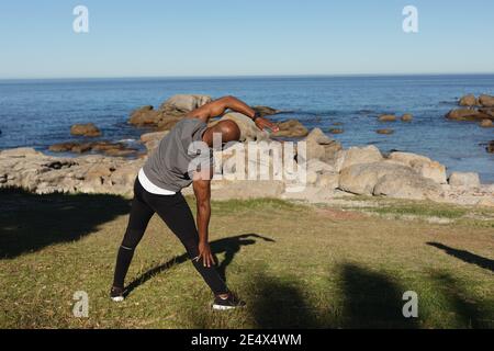 Rear view of fit senior african american man exercising outdoors by the sea stretching. healthy retirement outdoor fitness lifestyle. Stock Photo