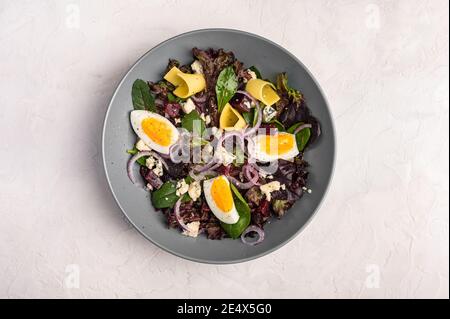Top view homemade salad of chicken eggs, boiled beetroot, cheese, arugula and basil with olive oil on a light background, copy space Stock Photo