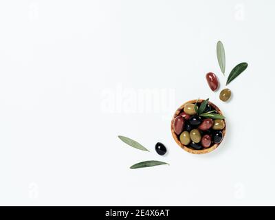 Olives tree leaves and fruits on white background. Small bowl with green, black and red kalamata olives, top view or flat lay. Olives isolated on white with copy space Stock Photo