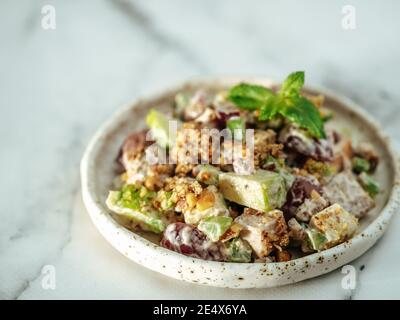 Waldorf salad with copy space. American fruit and nut salad with apples, celery, grapes, chicken meat, dressed mayonnaise. Craft plate with ready-to-eat waldorf salad on white marble background Stock Photo