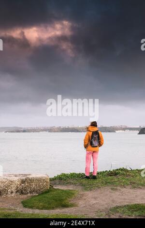 A female walker standing on the coastline and gazing out over Newquay Bay in Cornwall. Stock Photo