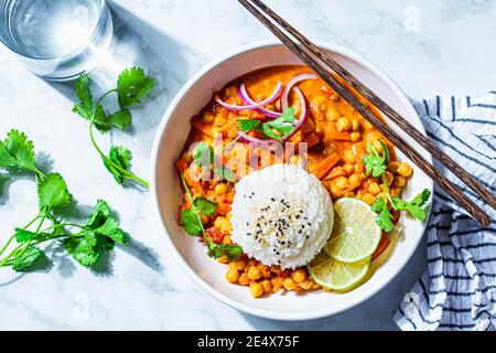 Vegan chickpea curry with rice and cilantro in a white bowl, white marble background. Indian cuisine concept. Stock Photo