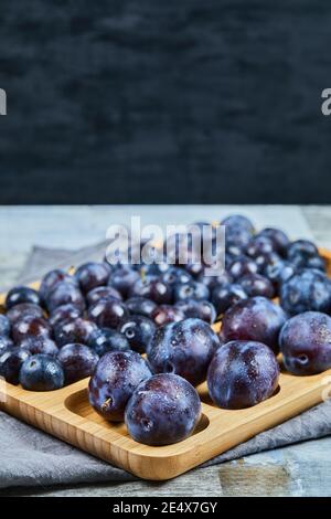Garden plums on wooden platter and on dark background Stock Photo