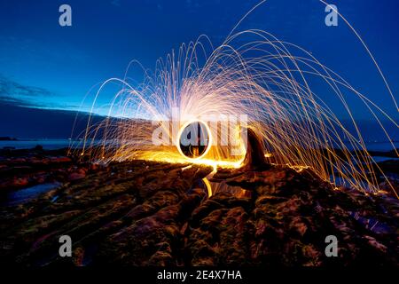 Amazing fire steel wool. Fire spinning circles with steel wool on the rock and beach Stock Photo