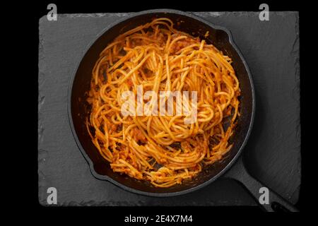 Spaghetti bolognese cooked in a cast iron frying pan. On a black background Stock Photo