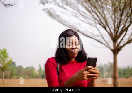 young black beautiful lady standing and using her smart phone in the park Stock Photo