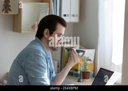 Concentrated young businessman freelancer dictating voice notes using phone recorder Stock Photo