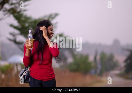 young beautiful african lady standing in a garden and holding a bottle of drink Stock Photo