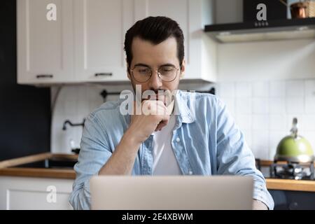 Doubtful man working from home pondering on data on screen Stock Photo